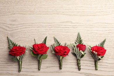 Many stylish red boutonnieres on light wooden table, flat lay. Space for text