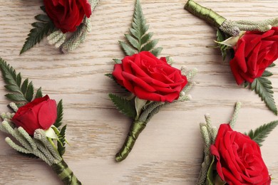 Many stylish red boutonnieres on light wooden table, flat lay