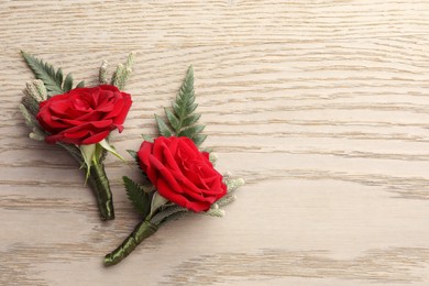 Photo of Two stylish red boutonnieres on light wooden table, top view. Space for text