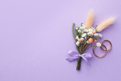 Small stylish boutonniere and rings on violet background, flat lay. Space for text