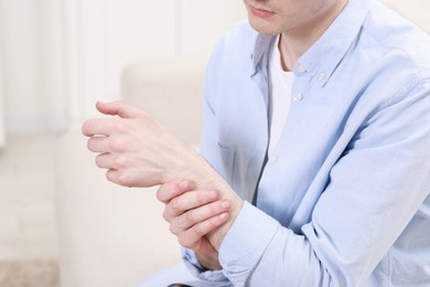 Photo of Man suffering from pain in hand on sofa indoors, closeup