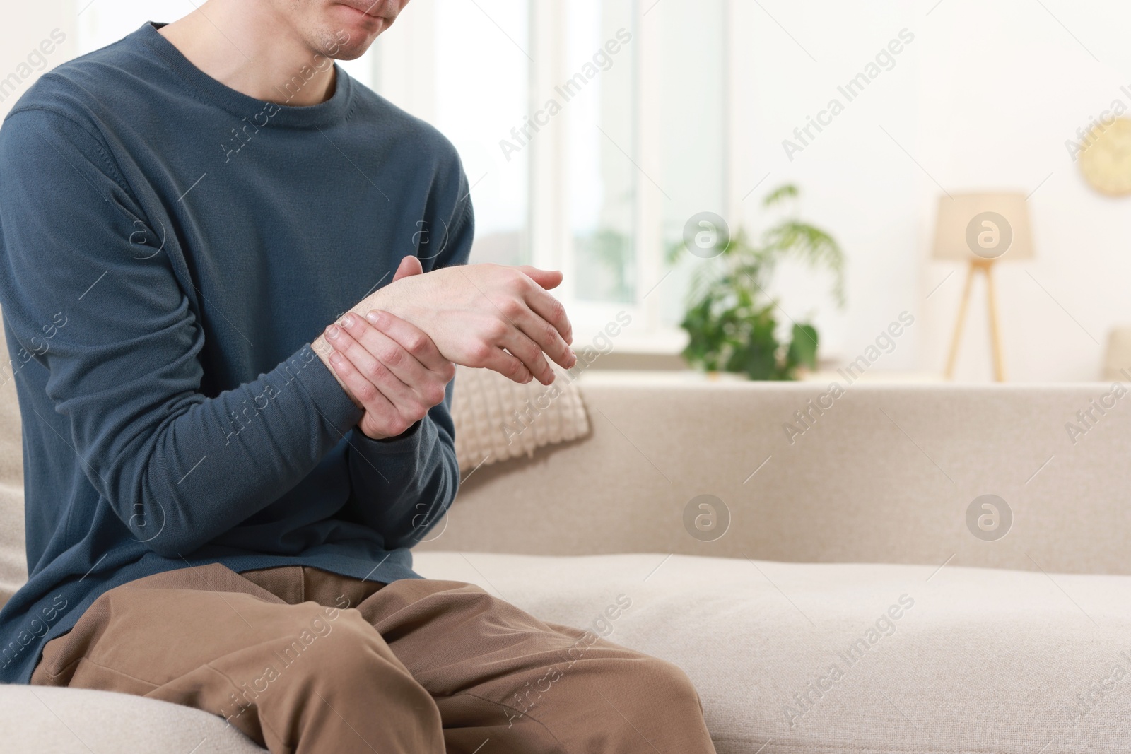 Photo of Man suffering from pain in hand on sofa indoors, closeup. Space for text