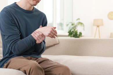 Man suffering from pain in hand on sofa indoors, closeup. Space for text