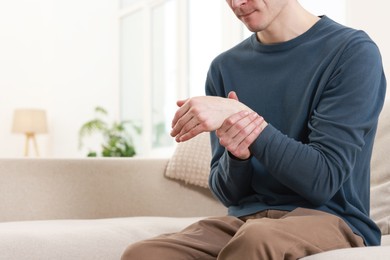 Man suffering from pain in hand on sofa indoors, closeup. Space for text