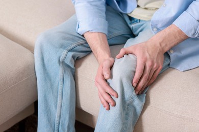 Man suffering from knee pain on sofa indoors, closeup