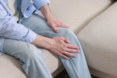 Man suffering from knee pain on sofa indoors, closeup