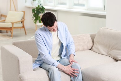 Man suffering from knee pain on sofa indoors