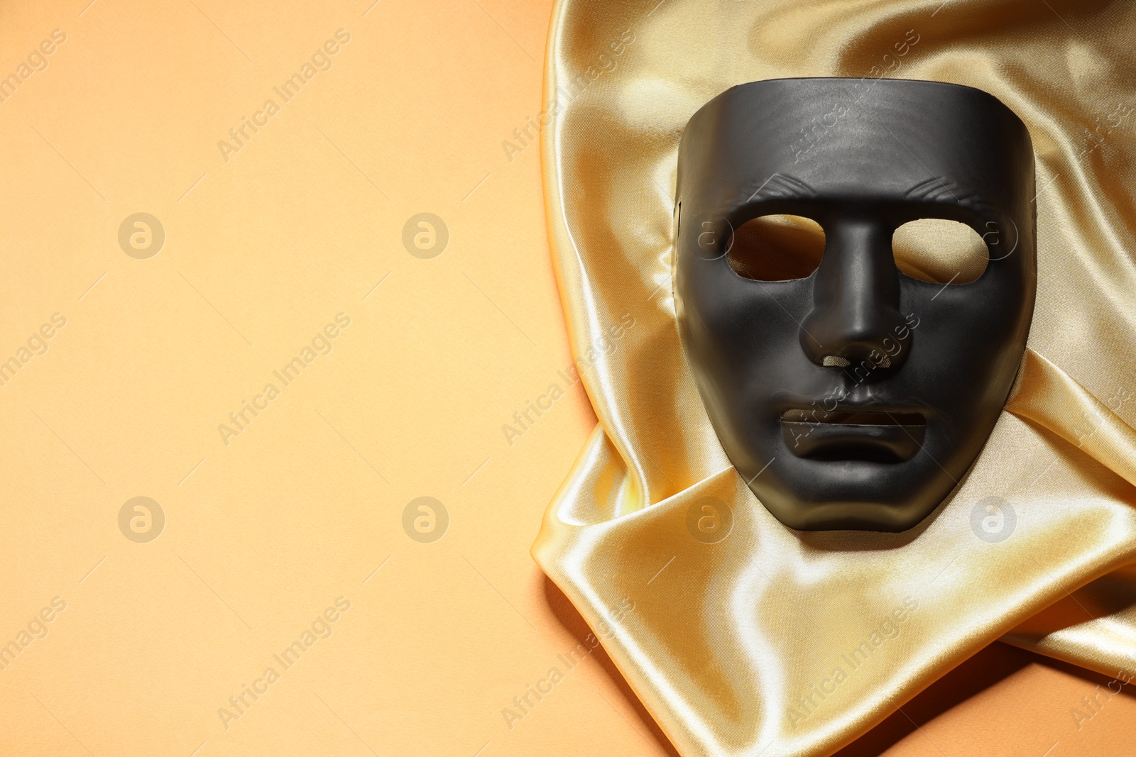 Photo of Theater arts. Black mask and golden fabric on pale orange background, top view. Space for text