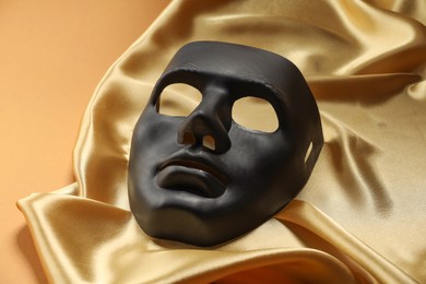 Photo of Theater arts. Black mask and golden fabric on pale orange background, closeup