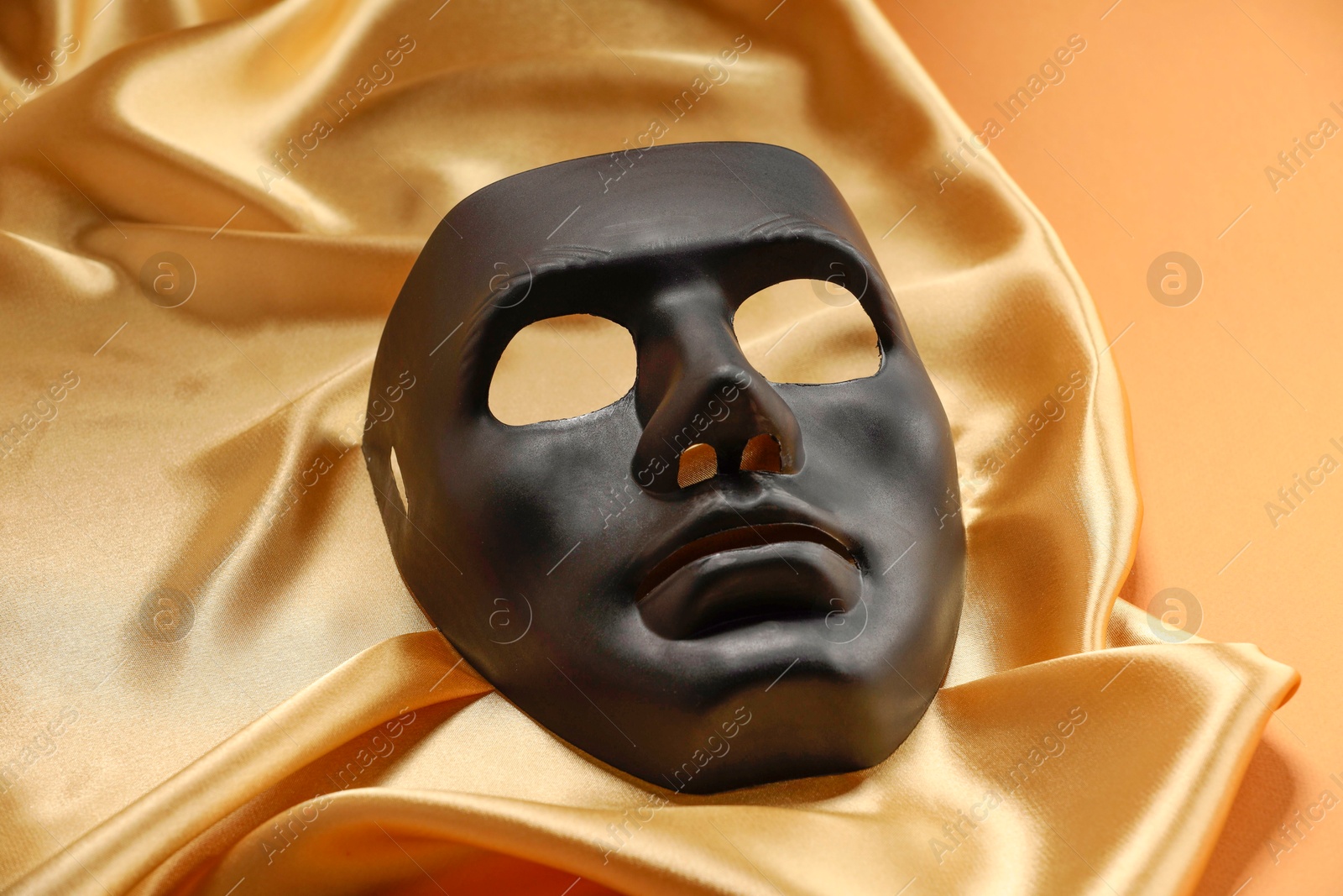 Photo of Theater arts. Black mask and golden fabric on pale orange background, closeup