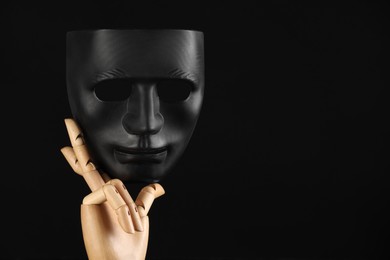 Wooden mannequin hand holding plastic mask on black background, space for text. Theatrical performance