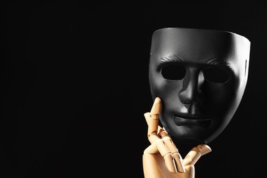 Photo of Wooden mannequin hand holding plastic mask on black background, space for text. Theatrical performance