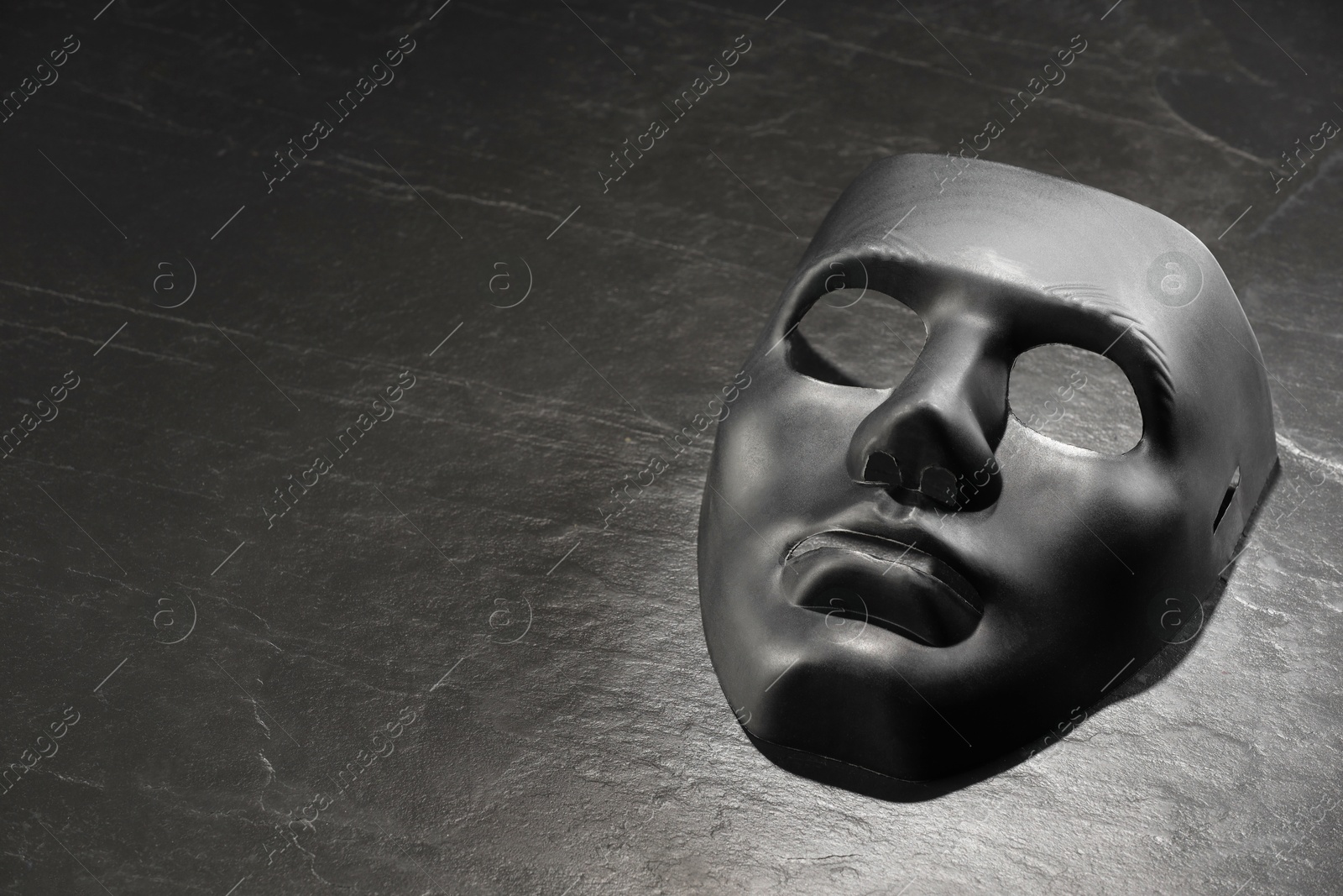 Photo of Plastic face mask on black slate surface, space for text. Theatrical performance