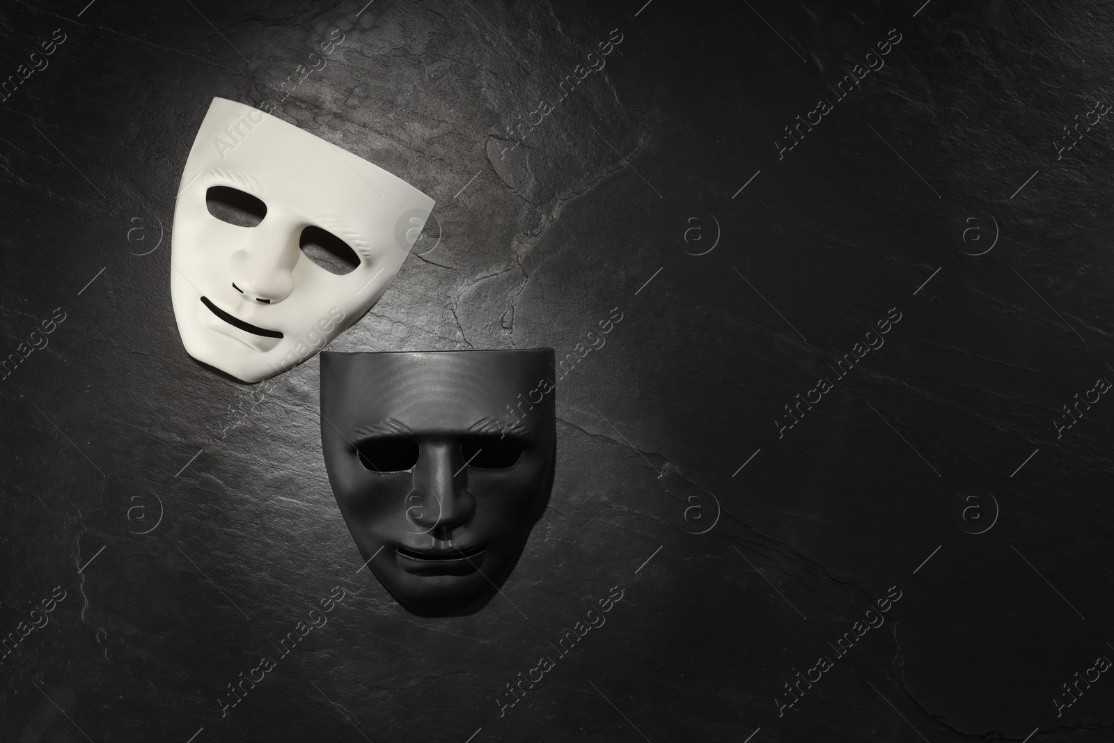 Photo of Plastic face masks on black slate surface, top view and space for text. Theatrical performance