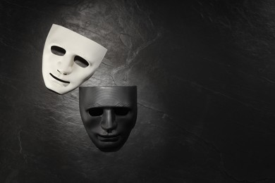 Plastic face masks on black slate surface, top view and space for text. Theatrical performance