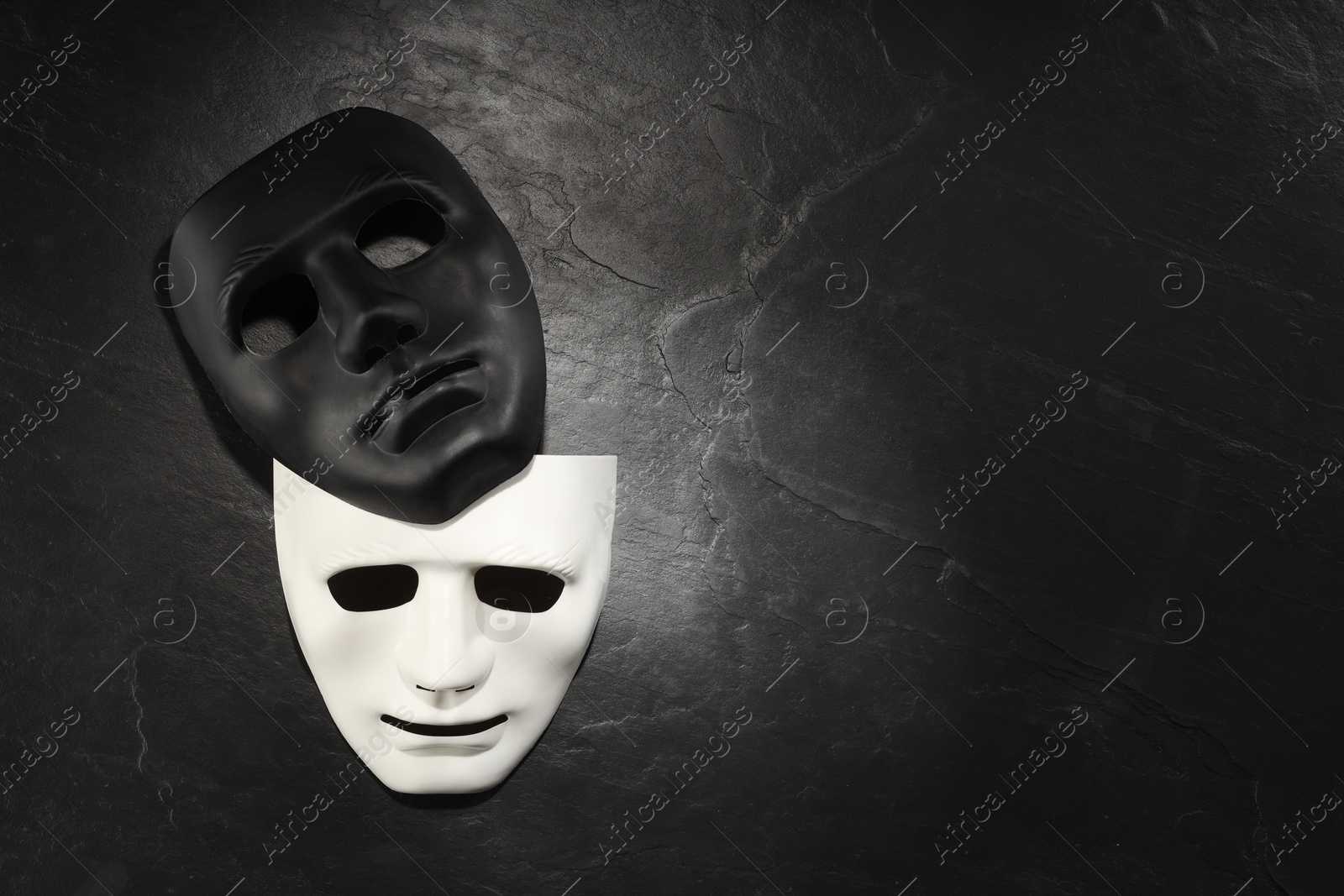 Photo of Plastic face masks on black slate surface, top view and space for text. Theatrical performance