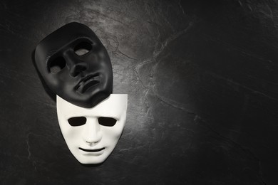 Plastic face masks on black slate surface, top view and space for text. Theatrical performance