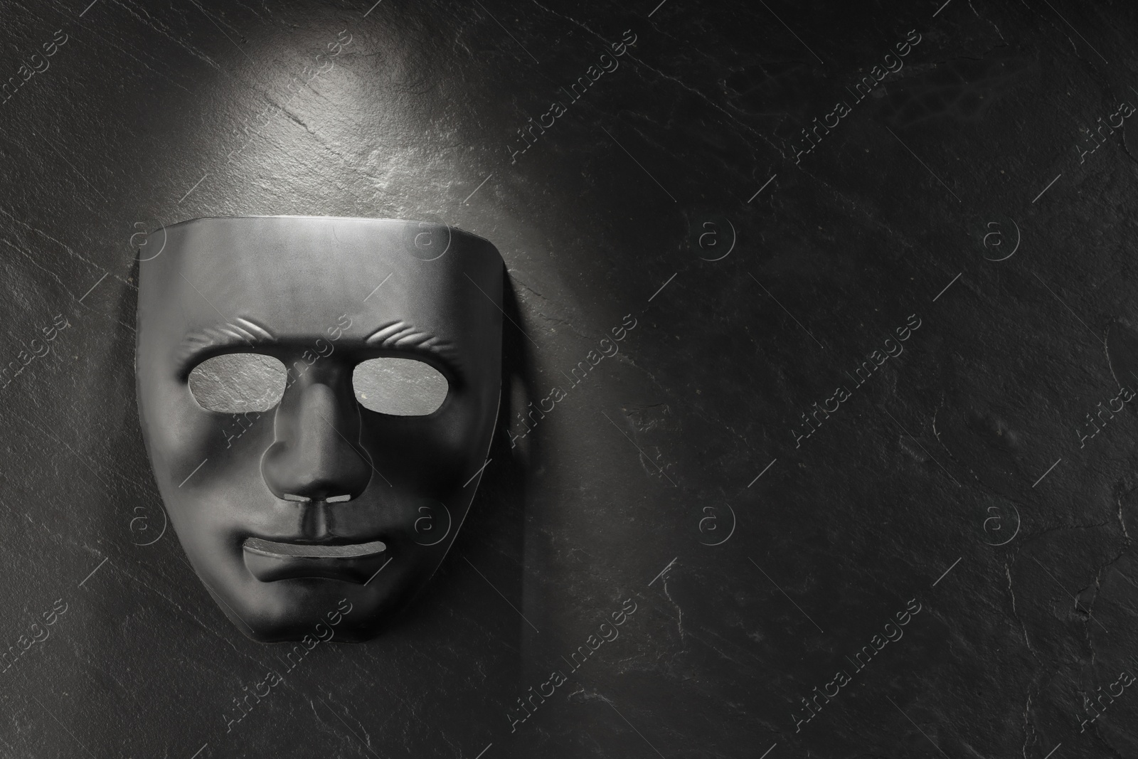 Photo of Plastic face mask on black slate surface, top view and space for text. Theatrical performance