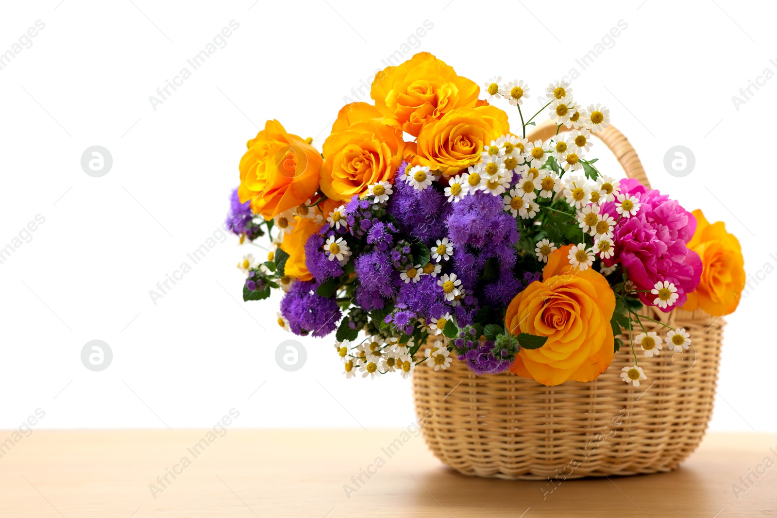 Photo of Wicker basket with beautiful flowers on light wooden table, space for text