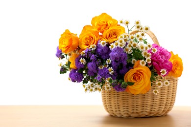 Wicker basket with beautiful flowers on light wooden table, space for text