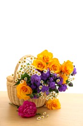 Photo of Wicker basket with beautiful flowers on light wooden table, space for text