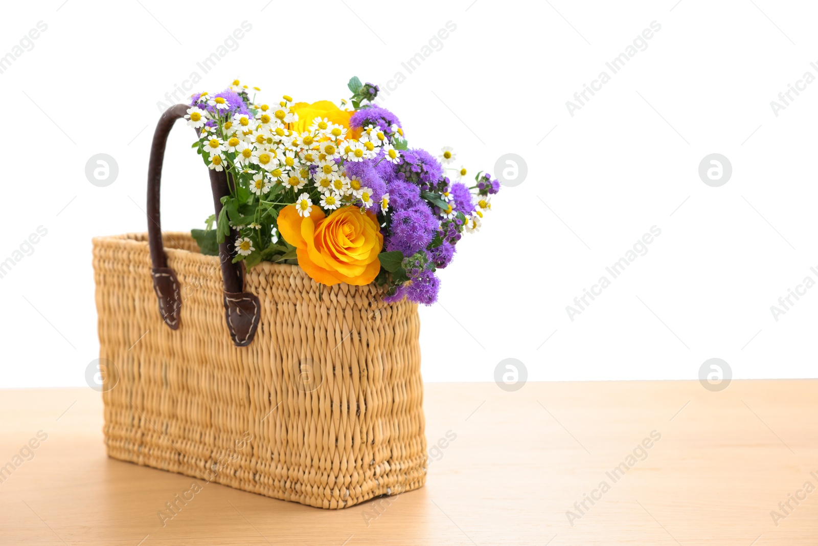 Photo of Wicker basket with beautiful flowers on light wooden table, space for text