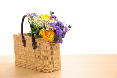 Photo of Wicker basket with beautiful flowers on light wooden table, space for text