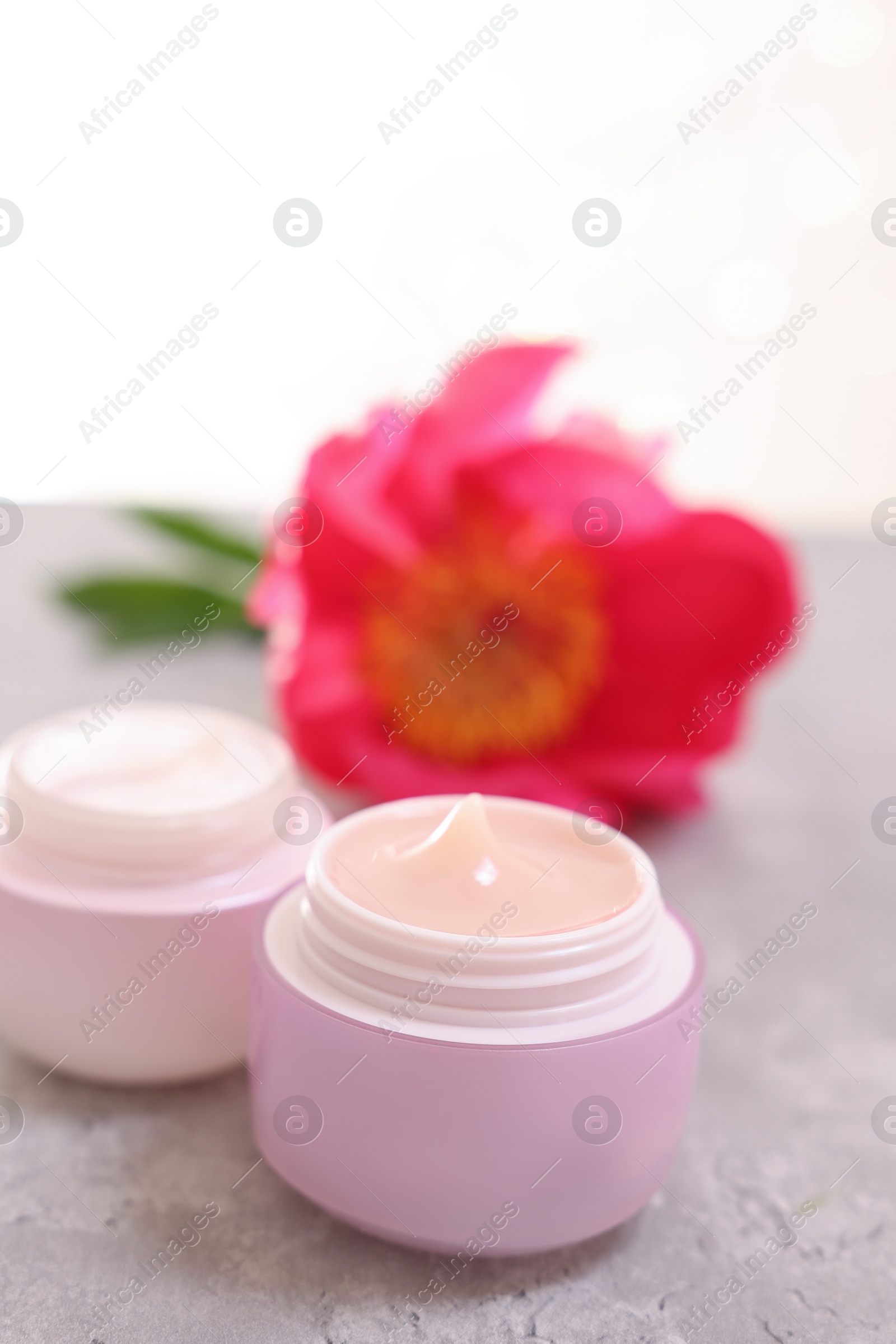 Photo of Jars of creams and peony flower on gray table against light background, closeup