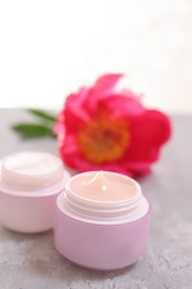 Jars of creams and peony flower on gray table against light background, closeup