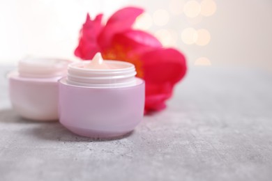 Photo of Jars of creams and peony flower on gray table against light background, closeup. Space for text