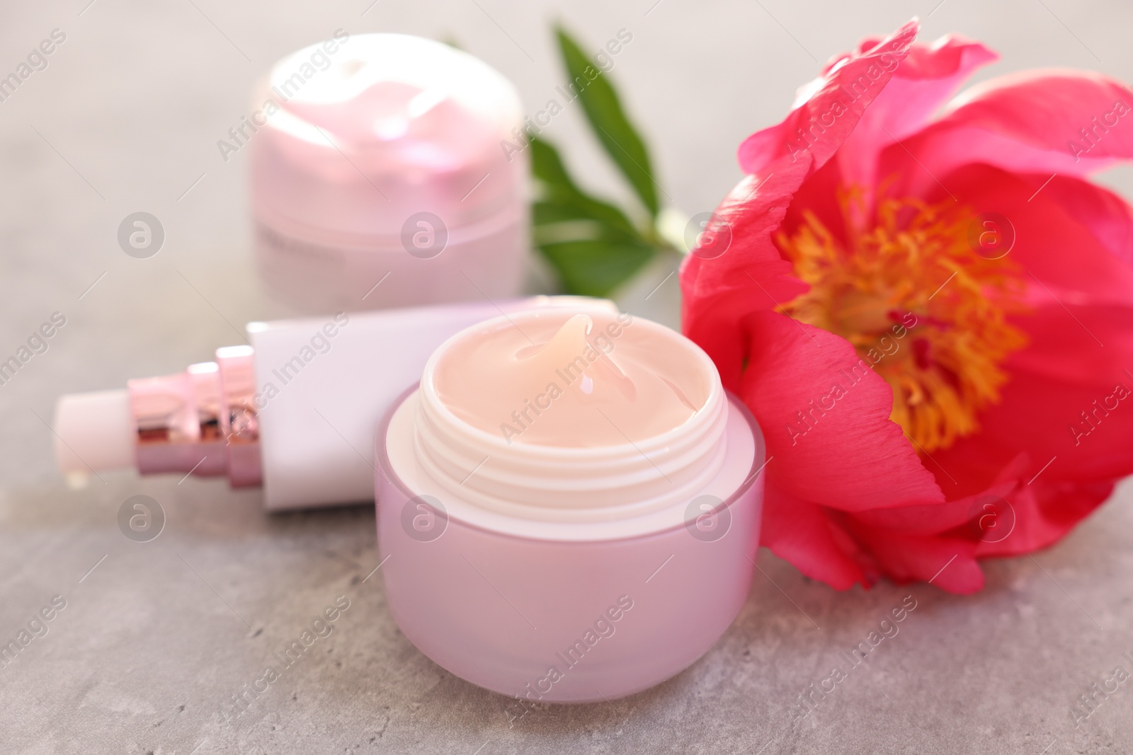 Photo of Set of different cosmetic products and peony flower on gray table, closeup