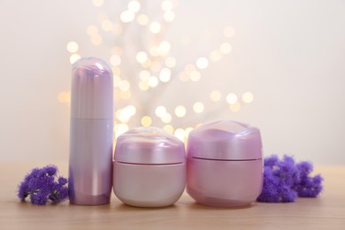 Photo of Set of different cosmetic products and ageratum flowers on wooden table against light background with blurred lights