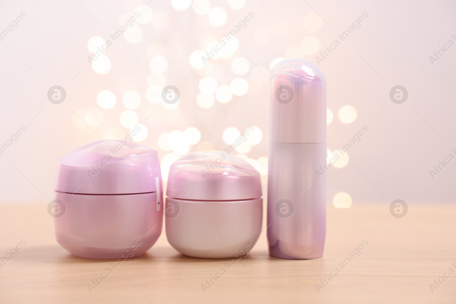 Photo of Set of different cosmetic products on wooden table against light background with blurred lights