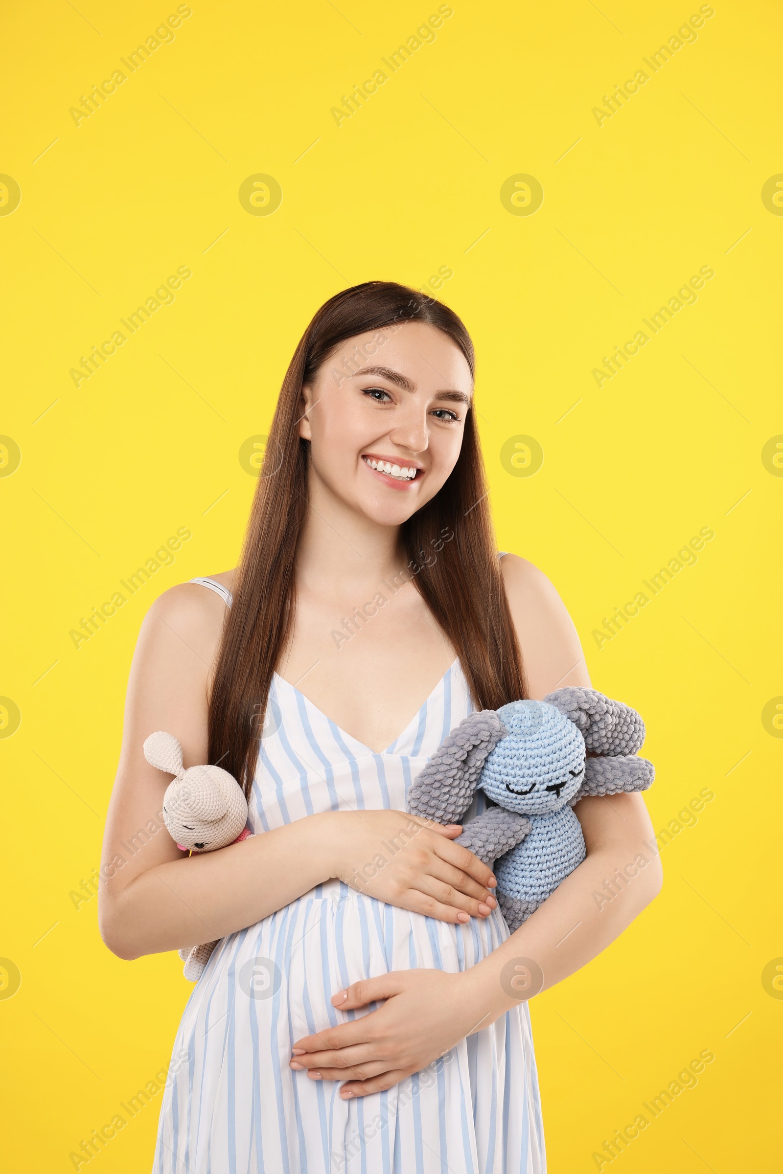 Photo of Expecting twins. Pregnant woman holding two toys on yellow background