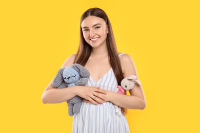 Photo of Expecting twins. Pregnant woman holding two toys on yellow background