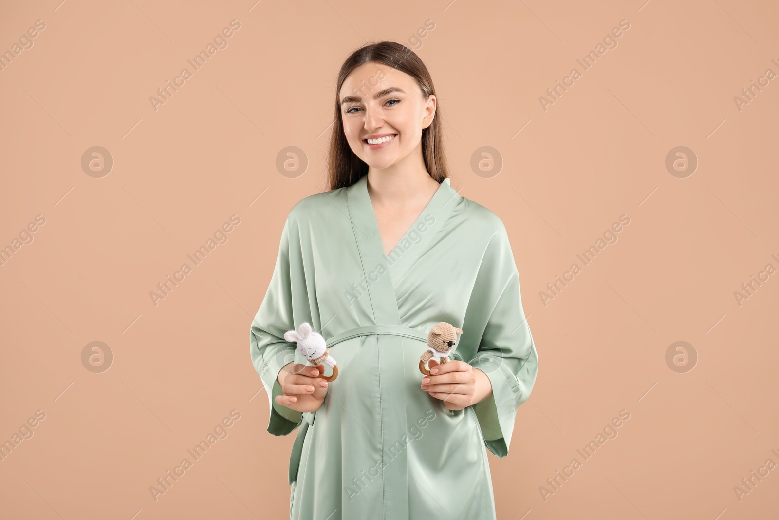 Photo of Expecting twins. Pregnant woman holding two toys on light brown background