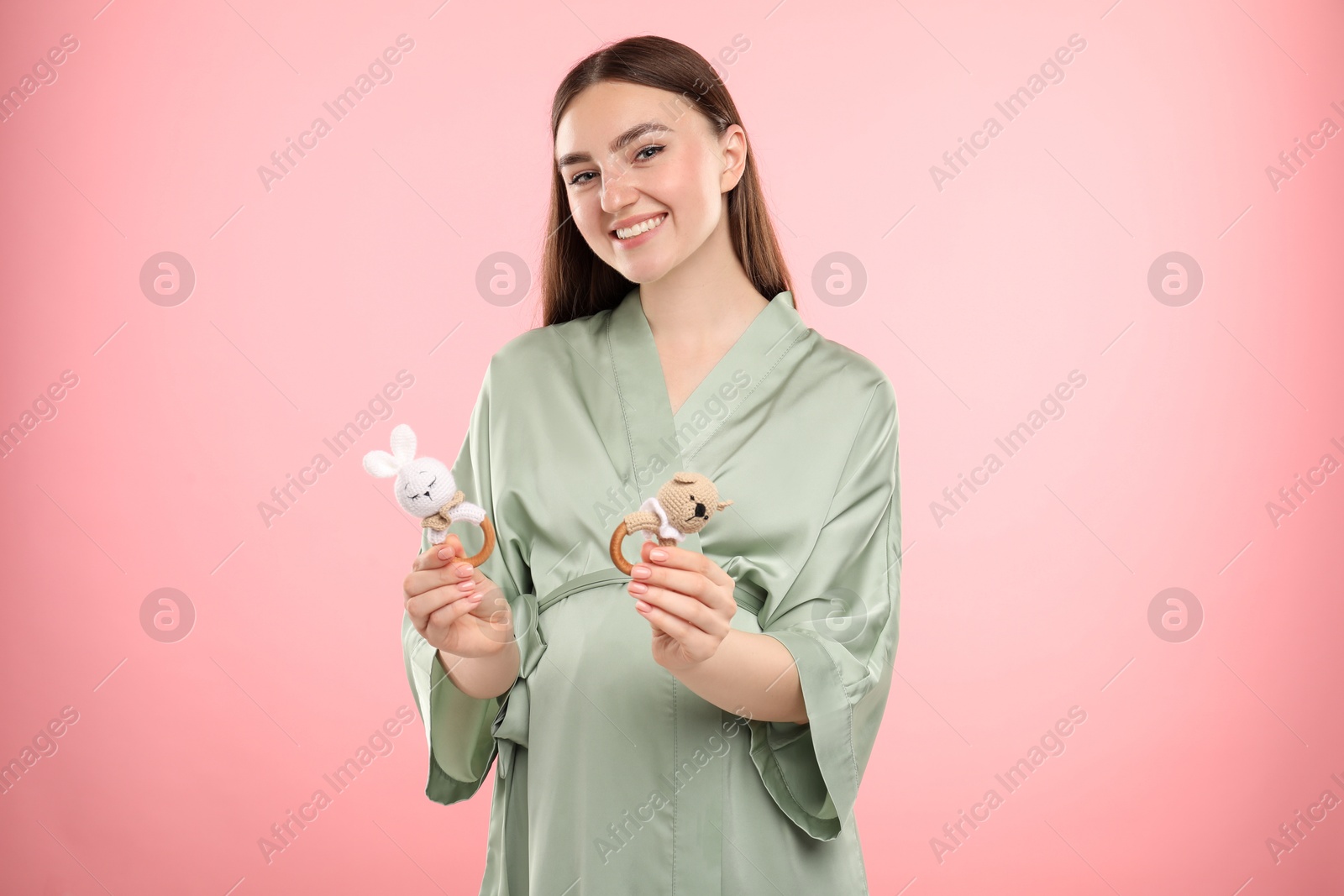 Photo of Expecting twins. Pregnant woman holding two toys on pink background