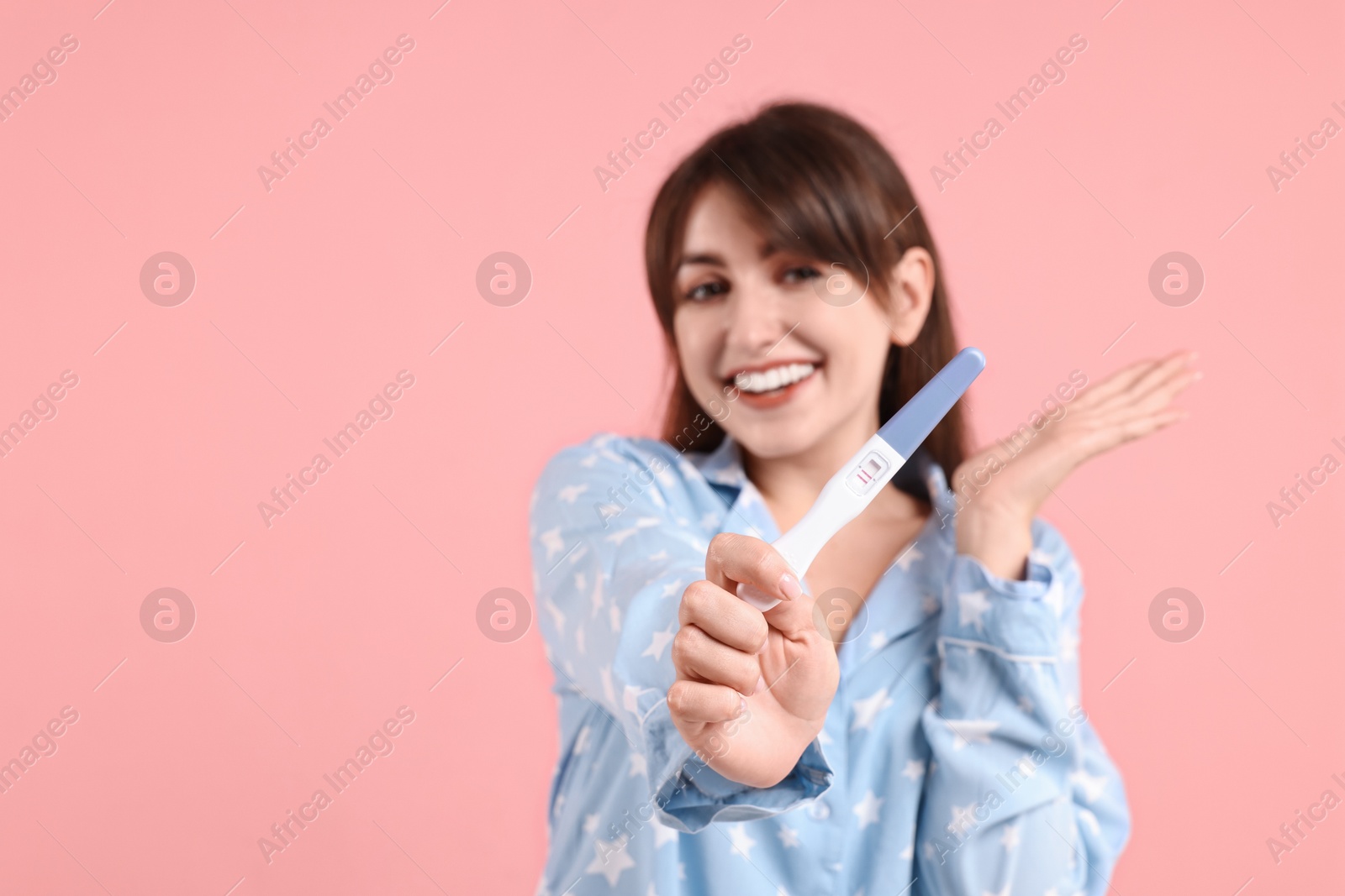 Photo of Happy young woman with pregnancy test on pink background, space for text