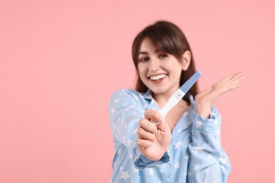 Happy young woman with pregnancy test on pink background, space for text