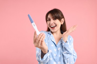 Photo of Happy young woman with pregnancy test on pink background