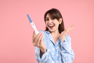 Happy young woman with pregnancy test on pink background