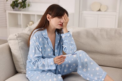 Photo of Worried young woman with pregnancy test on sofa at home