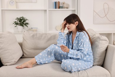 Photo of Worried young woman with pregnancy test on sofa at home