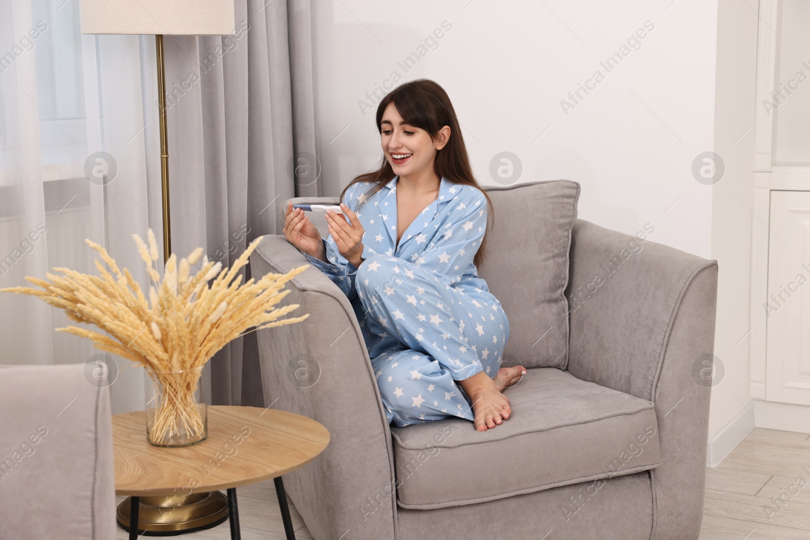 Photo of Happy young woman with pregnancy test on sofa at home