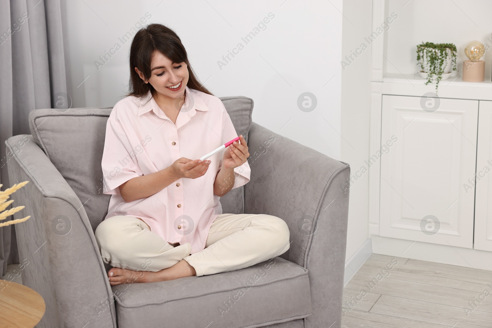 Photo of Happy young woman with pregnancy test on sofa at home, space for text