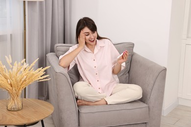 Happy young woman with pregnancy test on sofa at home