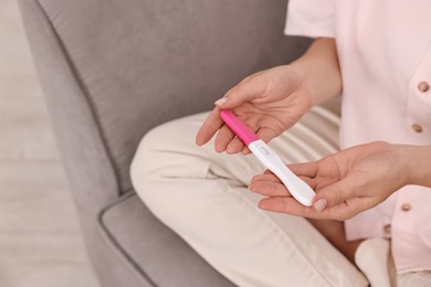 Photo of Young woman with pregnancy test on sofa at home, closeup