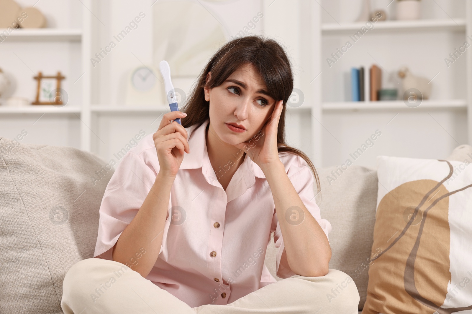 Photo of Worried young woman with pregnancy test on sofa at home