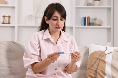 Photo of Worried young woman with pregnancy test on sofa at home