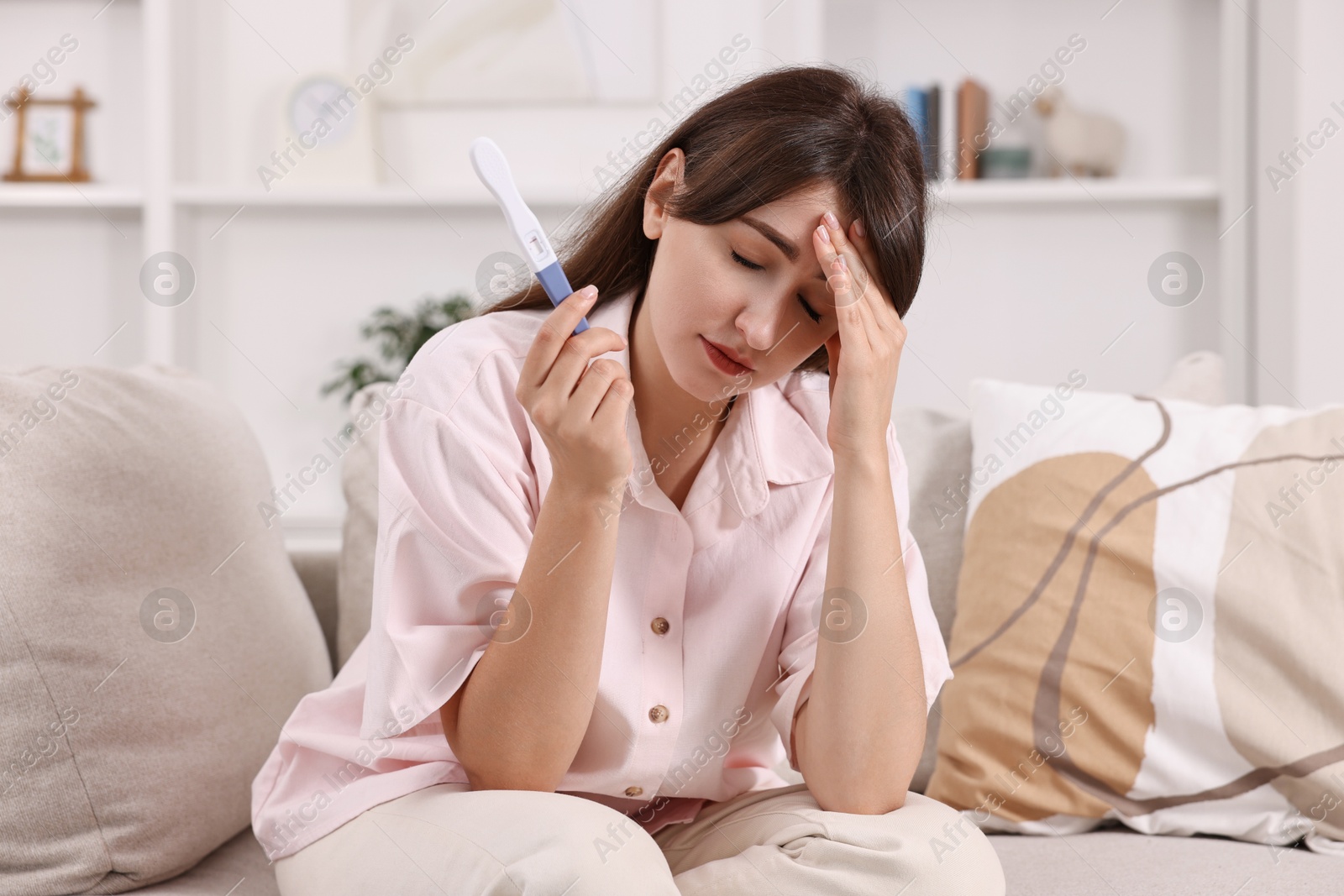 Photo of Worried young woman with pregnancy test on sofa at home